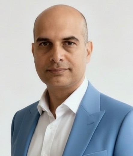 En partant de l'image fournie, supprimez le gilet bleu que porte l'homme pour laisser appara?tre la chemise blanche qui se trouve en dessous. L'homme doit donc porter une veste de costume bleue ouverte sur une chemise blanche, mais sans le gilet. Conservez la m?me personne, la m?me pose, le m?me arri?re-plan et le m?me style r?aliste.
